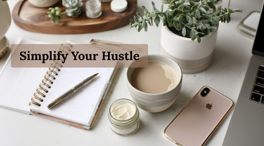 Flat lay of a notebook, pen, cup of coffee, small tallow jar, iPhone, and potted plant with the text “Simplify Your Hustle.”