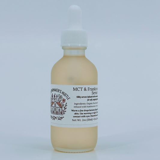Glass dropper bottle of MCT & Frankincense Serum from The Homemaker’s Hustle. The label includes a farmhouse illustration and text describing a silky serum infused with frankincense resin. Net weight 2 oz.