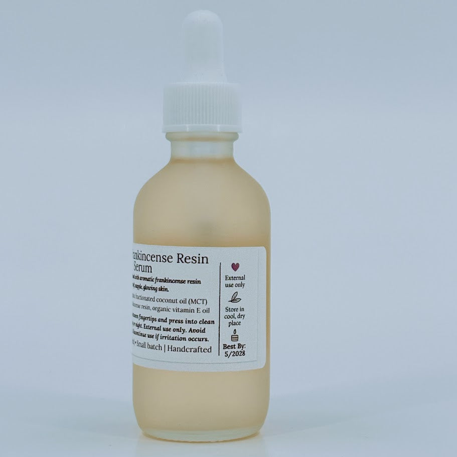 Glass dropper bottle of MCT & Frankincense Serum from The Homemaker’s Hustle. The label includes a farmhouse illustration and text describing a silky serum infused with frankincense resin. Net weight 2 oz.