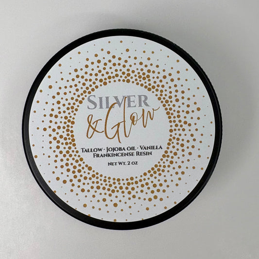 Round product label for Silver & Glow balm. The label features a white background with a gold dotted circular pattern. Text reads: ‘Silver & Glow. Tallow, Jojoba Oil, Vanilla, Frankincense Resin. Net Wt. 2 oz.